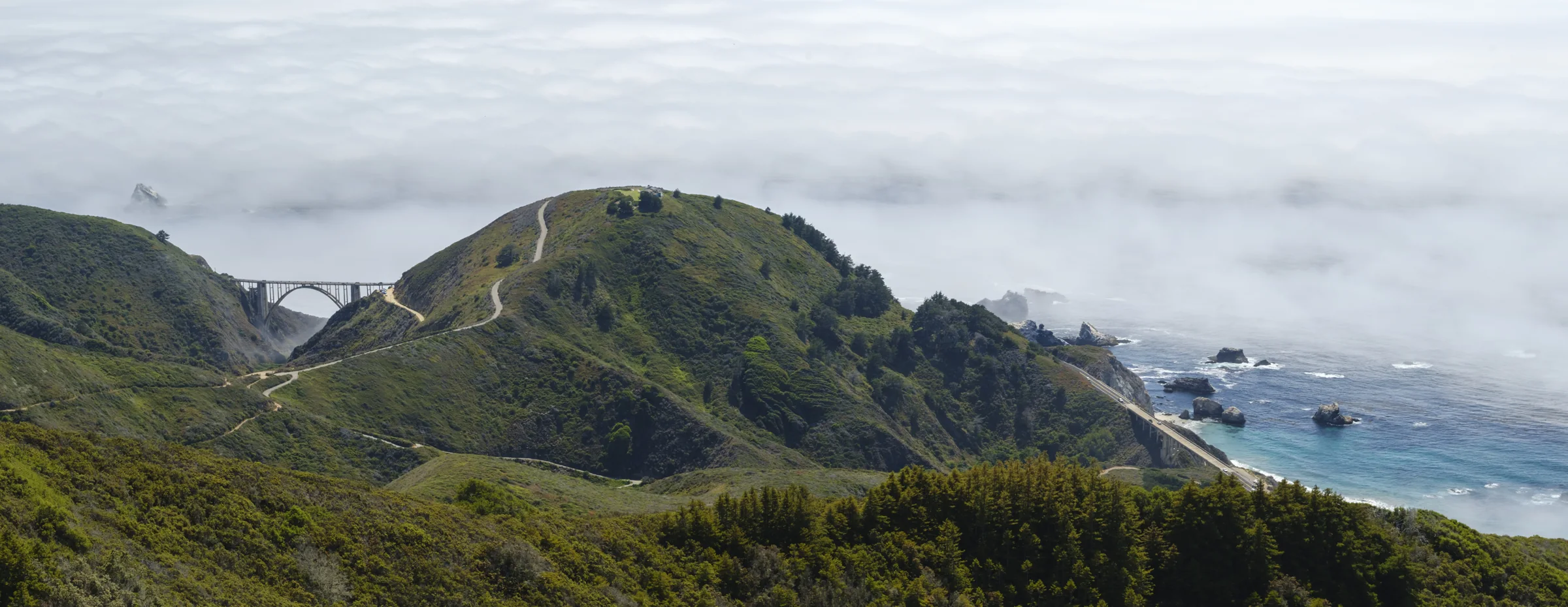 Rare panoramic view of both Bixby Creek Bridge and Rocky Creek Bridge in one frame from private land above the Old Coast Road, Big Sur, California, with the marine layer sitting on the Pacific below, by Manny Espinoza
