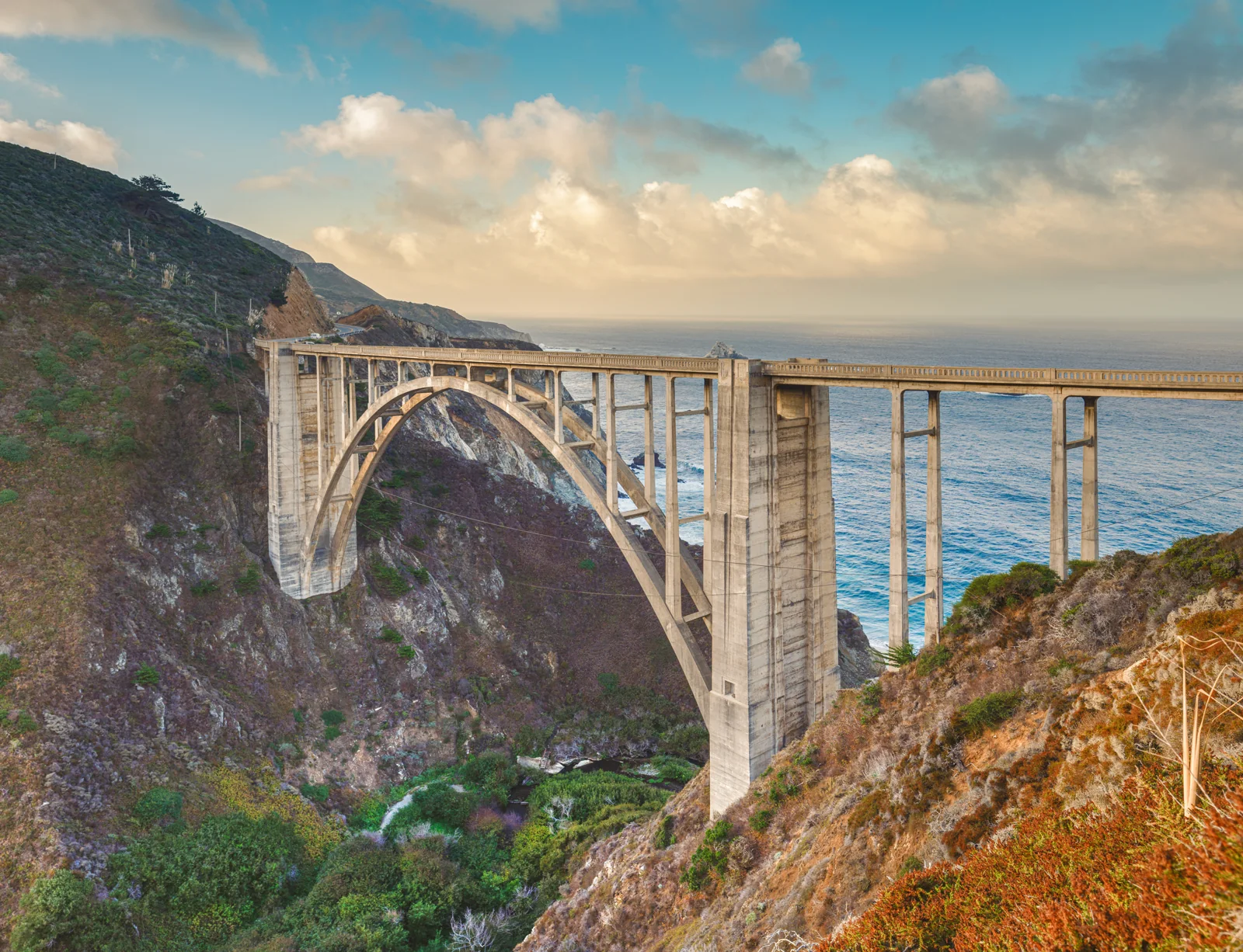 Close view of the Bixby Creek Bridge arch at last light, Big Sur, California, with the west face of the concrete glowing gold and the Pacific behind, fine art print by Manny Espinoza