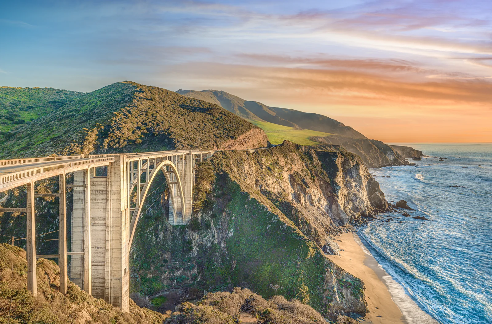 Bixby Creek Bridge at sunset from the Castle Rock Viewpoint, Big Sur, California, with the arch, green spring hills, the coastline running south and the beach at the creek mouth, fine art print by Manny Espinoza