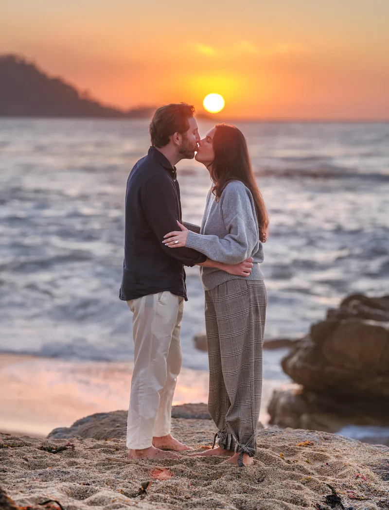 Couple kissing at sunset on the Carmel coast with her engagement ring visible, photographed by Manny Espinoza