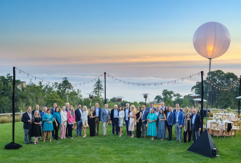 Corporate retreat dinner on a Big Sur lawn at dusk with a lit balloon and string lights, conference and event photography by Manny Espinoza