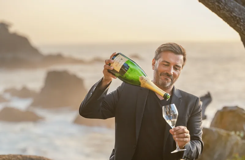 Man in a dark blazer pouring champagne on the Carmel coast at sunset, personal brand portrait by Manny Espinoza