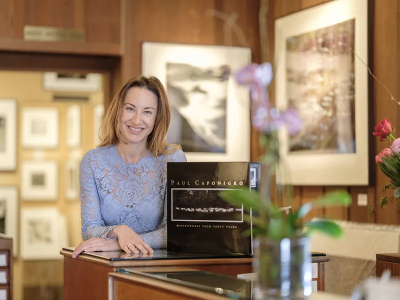 Gallery owner smiling behind the counter of her Carmel art gallery with framed prints behind her, business portrait by Manny Espinoza