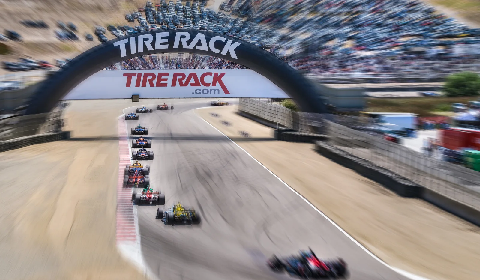 Race cars leaving the grid beneath a Tire Rack bridge, motorsport photography by Manny Espinoza