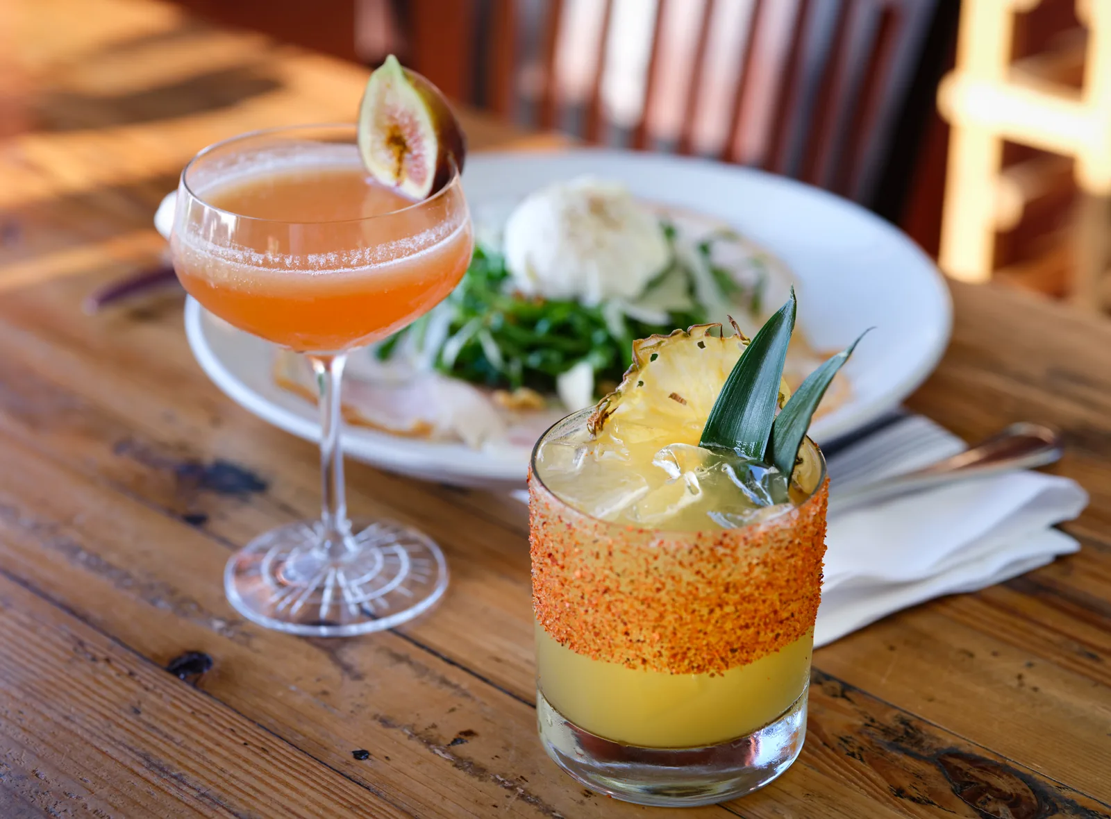Two craft cocktails beside a burrata and greens appetizer at Mezzaluna, restaurant photography by Manny Espinoza