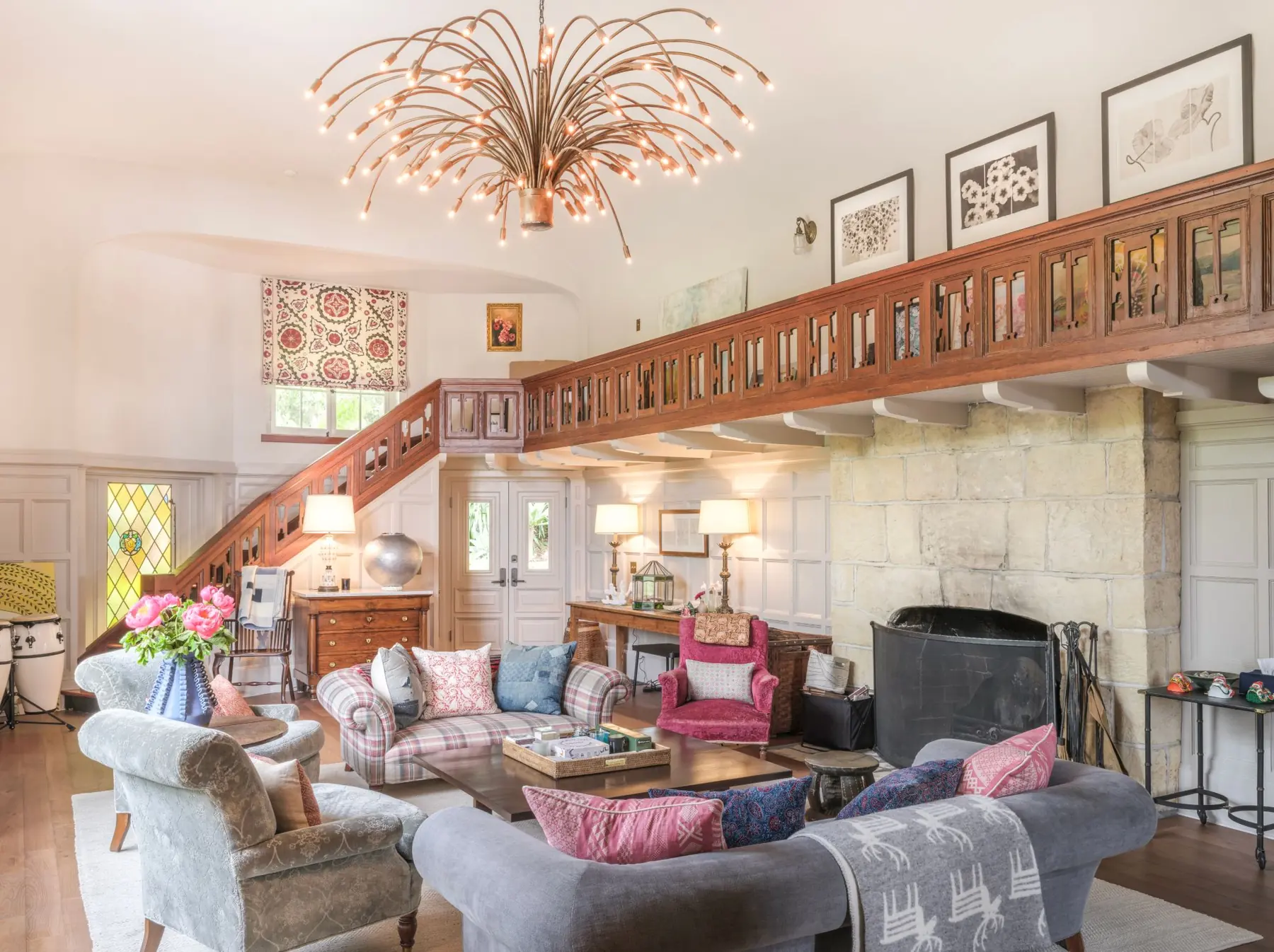 Great room of Seastone in the Carmel Highlands with interiors by Kathryn M. Ireland: double-height windows, carved wood gallery, limestone fireplace and a branching brass chandelier — interior photography by Manny Espinoza