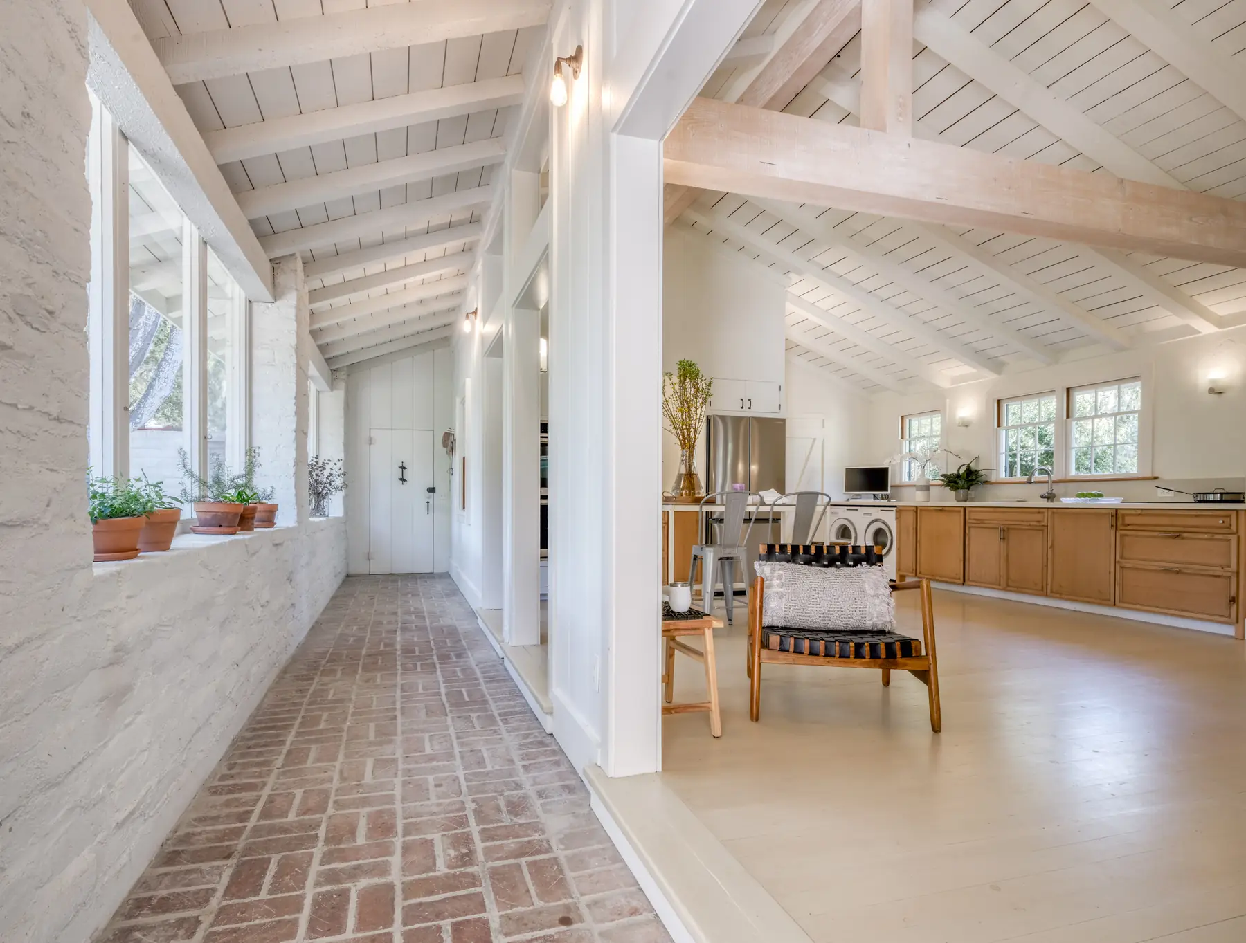 Brick-floored hallway with vaulted white beamed ceiling and windows to the garden in the Monterey adobe