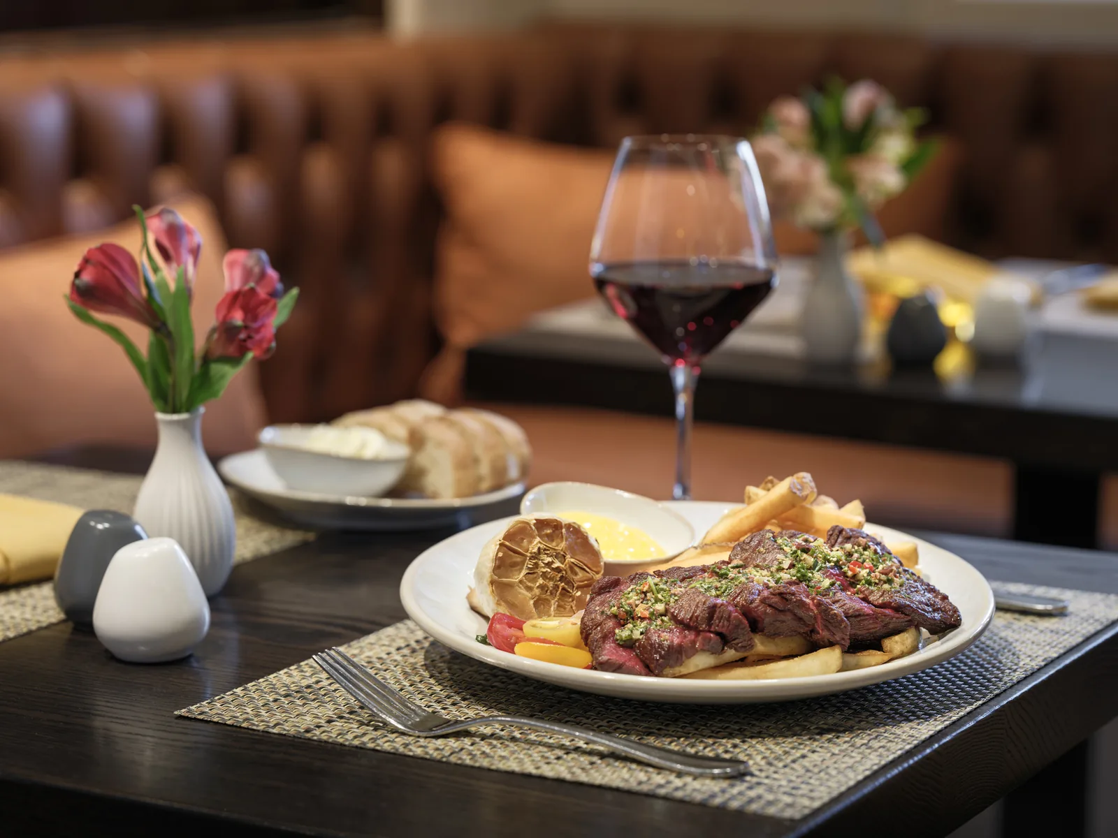 Steak dinner with tulips and a glass of red wine in a leather booth, restaurant food photography by Manny Espinoza