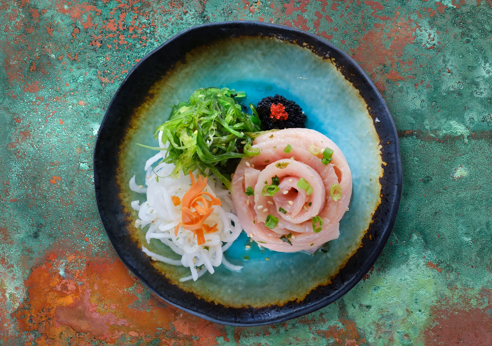 Overhead photograph of a sushi plate with caviar and pickled radish on a copper-glazed dish, restaurant food photography