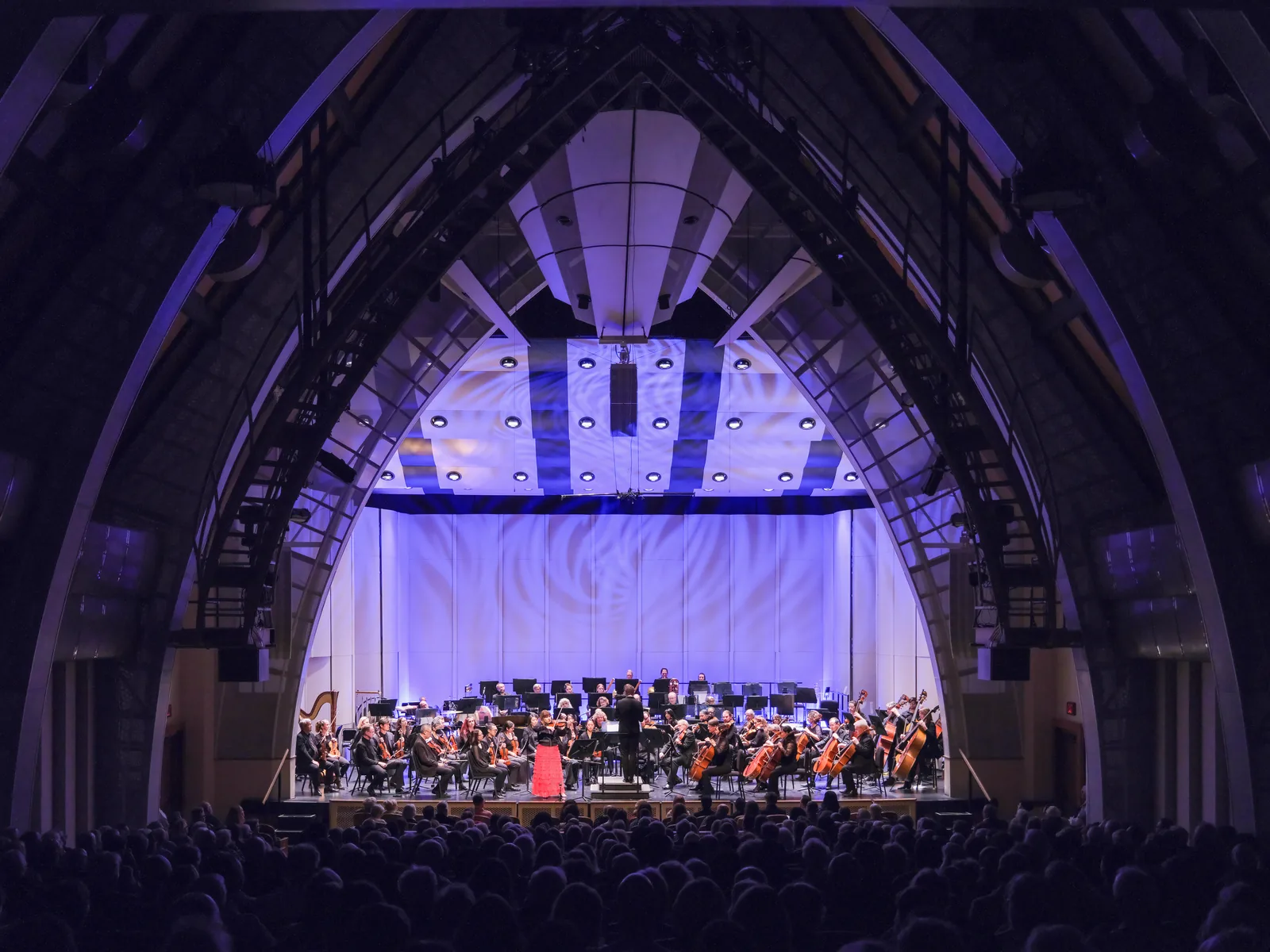 Symphony orchestra performing in an arched hall with a lit stage, concert photography by Manny Espinoza