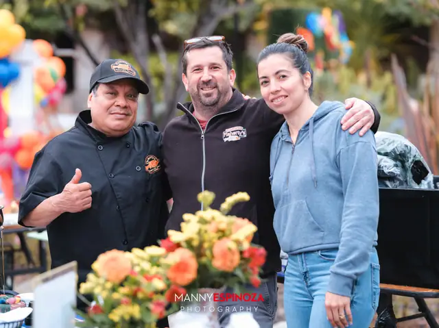 Chefs and a guest beside a bouquet of orange flowers at a food station at Taste of Carmel 2026