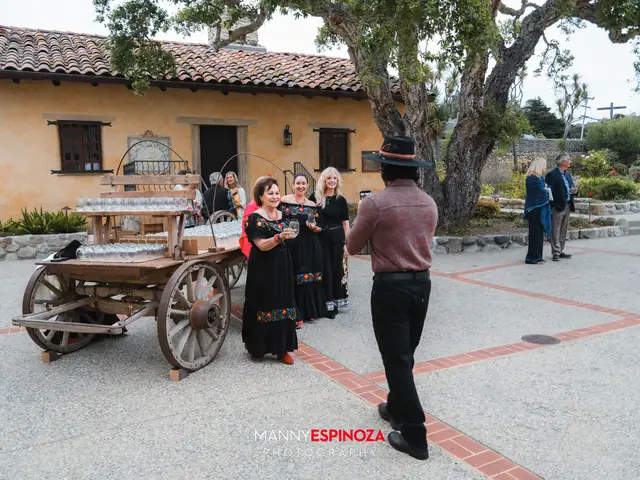 Women in traditional Mexican dresses beside a wooden wagon in the Carmel Mission courtyard at Taste of Carmel 2026