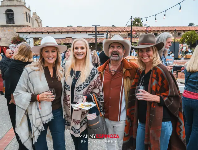 Four guests in ponchos and hats holding wine and small plates at Taste of Carmel 2026