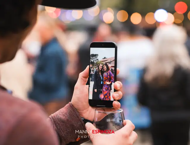 A guest photographing friends on a phone while holding a wine glass at Taste of Carmel 2026