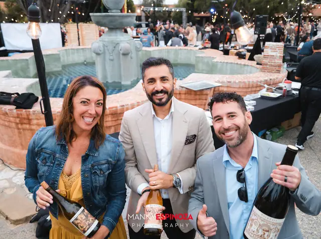 Three guests holding magnum bottles of wine in front of the Carmel Mission courtyard fountain at Taste of Carmel 2026