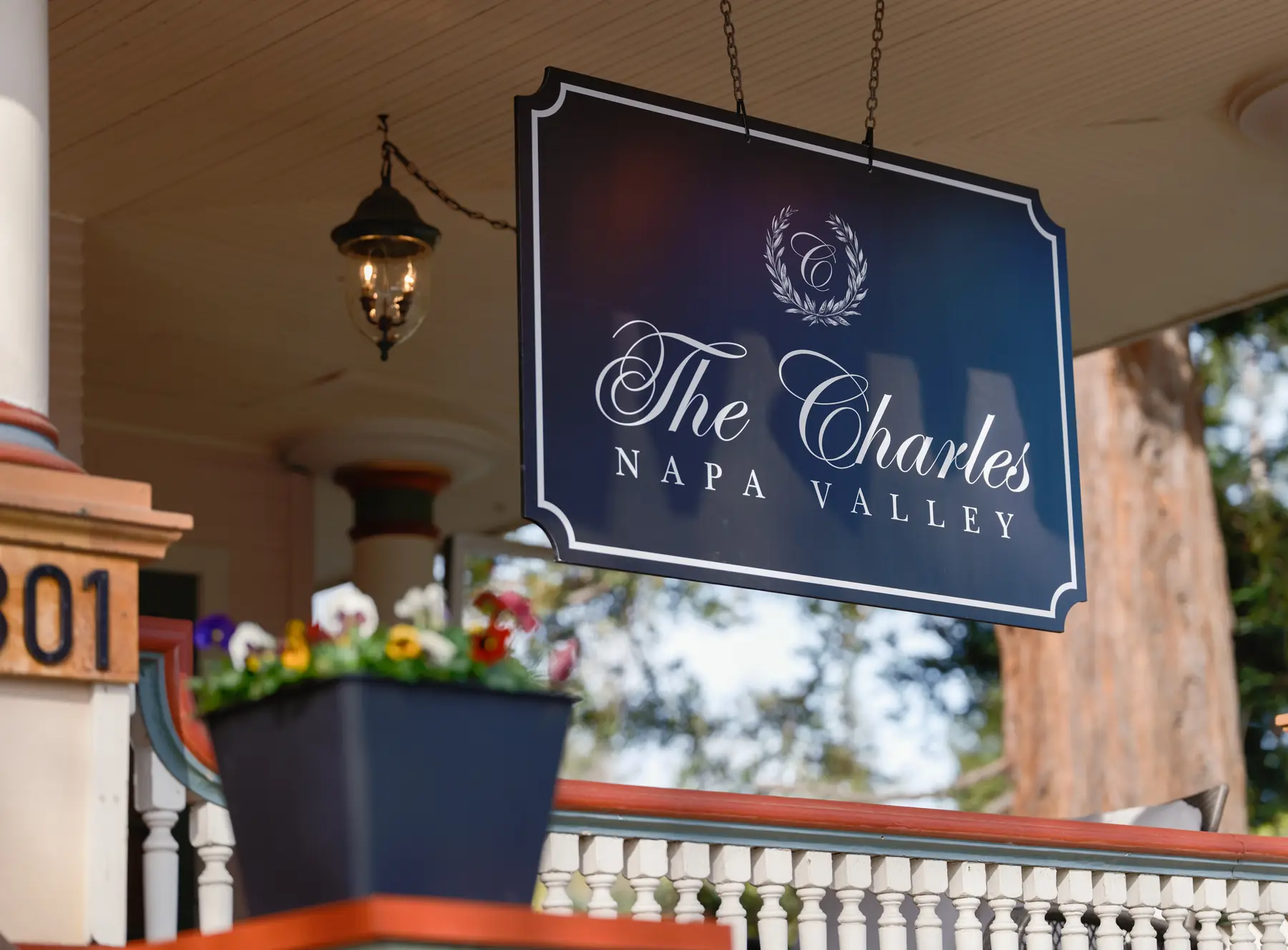 Hanging sign for The Charles Napa Valley with laurel wreath monogram above the covered porch entrance at 1301 Jefferson Street, Napa