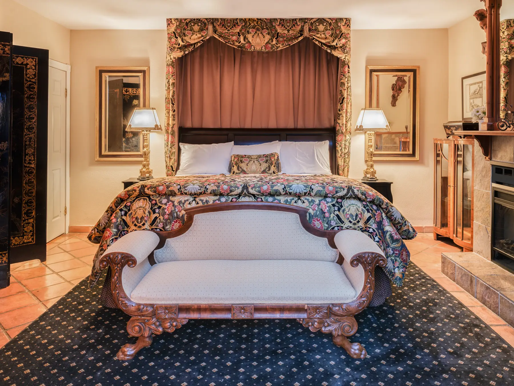 Guest room at The Charles Napa Valley with a floral canopy bed and carved antique settee on a navy patterned rug