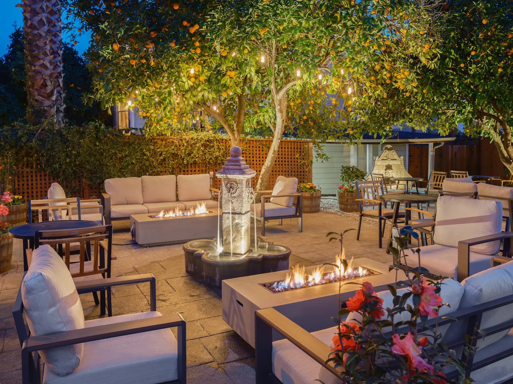 Patio seating with lit fire pits and string lights in citrus trees at The Charles Napa Valley, Napa, at dusk