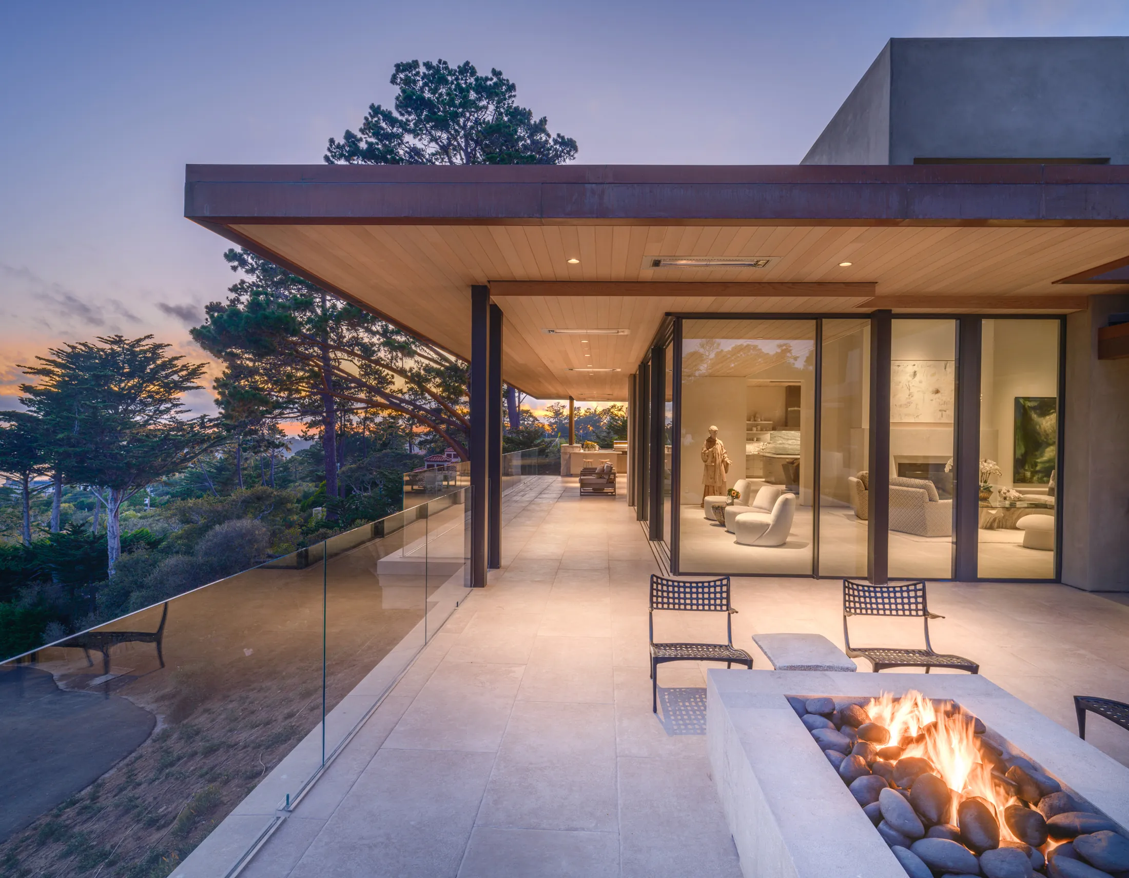 Covered terrace of The Edge at twilight, fire pit lit, interior glowing through glass, Pebble Beach