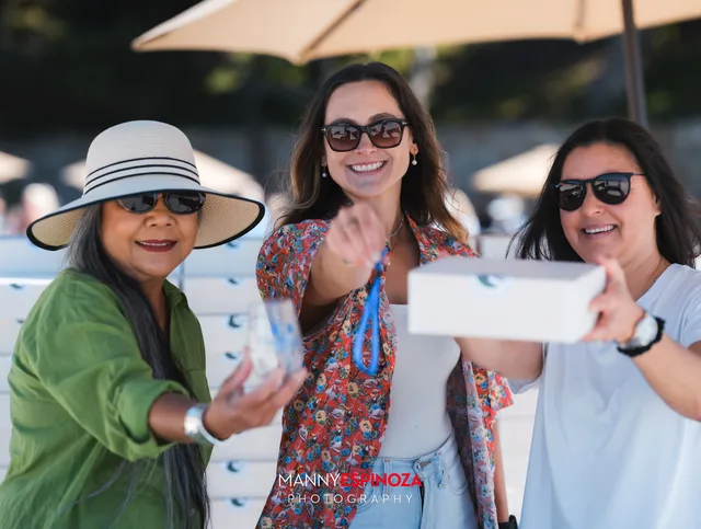 Three women, one in a white sun hat, sharing a box of bites at Walk for Freedom 2026 on Carmel Beach