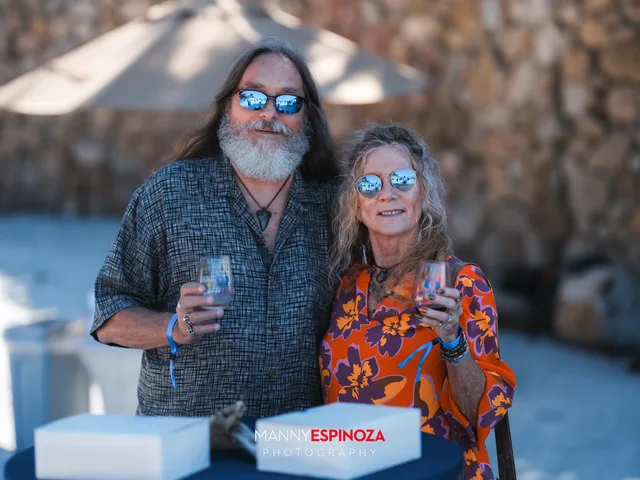 A couple in sunglasses with glasses of wine in front of the stone seawall at Walk for Freedom 2026 on Carmel Beach