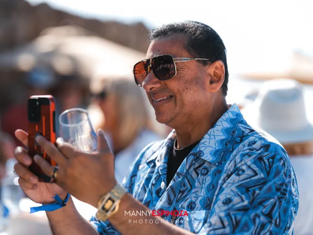 A guest in a blue print shirt filming the program on his phone at Walk for Freedom 2026 on Carmel Beach