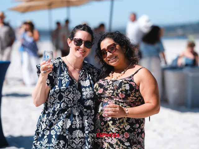 Two women in black floral dresses with glasses raised at Walk for Freedom 2026 on Carmel Beach