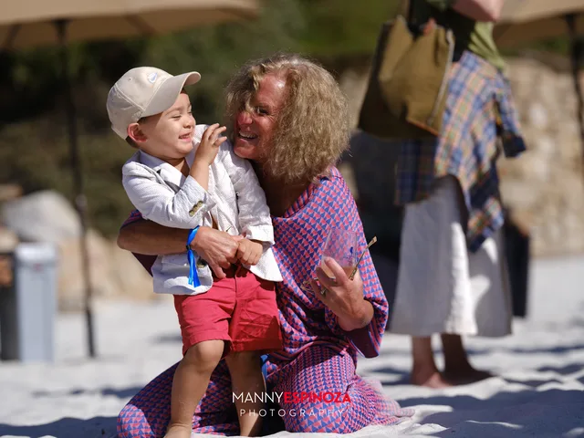 A grandmother lifting a toddler in a cap on the sand at Walk for Freedom 2026 on Carmel Beach
