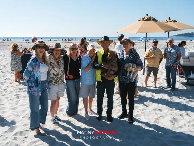 A group posing under the umbrellas, one guest holding a small dog at Walk for Freedom 2026 on Carmel Beach