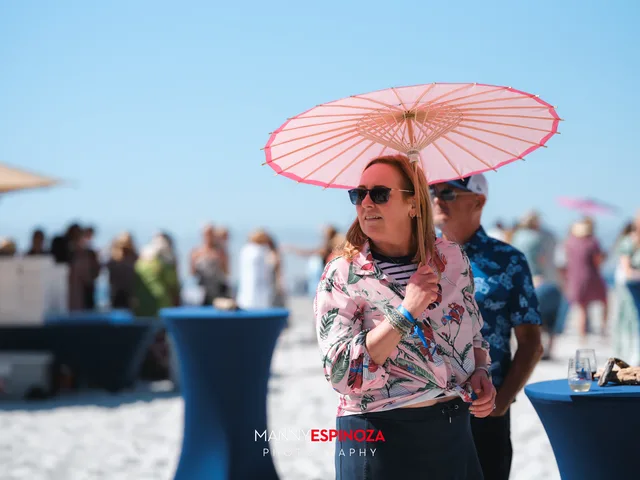 A guest shading under a pink paper parasol among the cocktail tables at Walk for Freedom 2026 on Carmel Beach