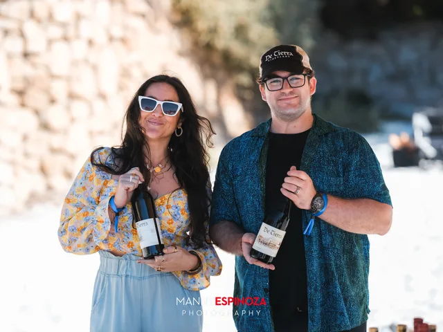 A couple holding up bottles at their pouring table beside the rocks at Walk for Freedom 2026 on Carmel Beach