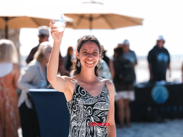 A woman in a black and white dress raising her glass at Walk for Freedom 2026 on Carmel Beach