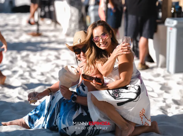 Two women sitting in the sand with glasses raised at Walk for Freedom 2026 on Carmel Beach