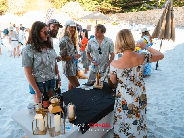 Guests chatting at a pouring table in the shade of the rocks at Walk for Freedom 2026 on Carmel Beach