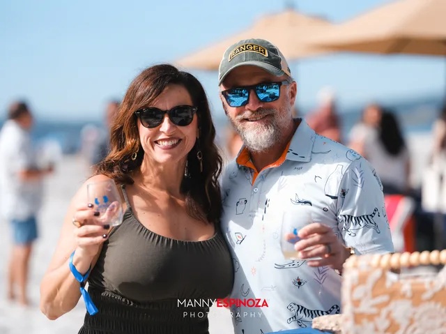 A couple in sunglasses and caps toasting on the sand at Walk for Freedom 2026 on Carmel Beach