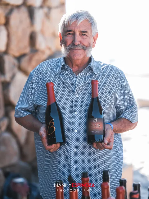 A pourer holding two bottles of red wine against the stone wall at Walk for Freedom 2026 on Carmel Beach