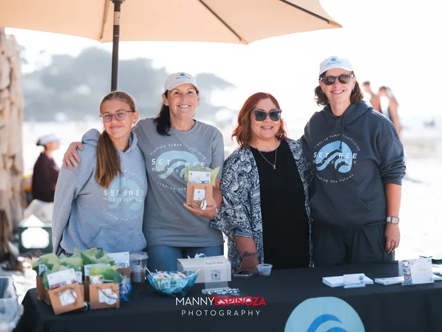 Four volunteers in matching sweatshirts at the welcome table under an umbrella at Walk for Freedom 2026 on Carmel Beach