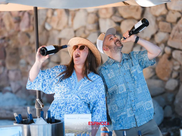 Two guests in blue clowning with wine bottles raised at a winery table at Walk for Freedom 2026 on Carmel Beach