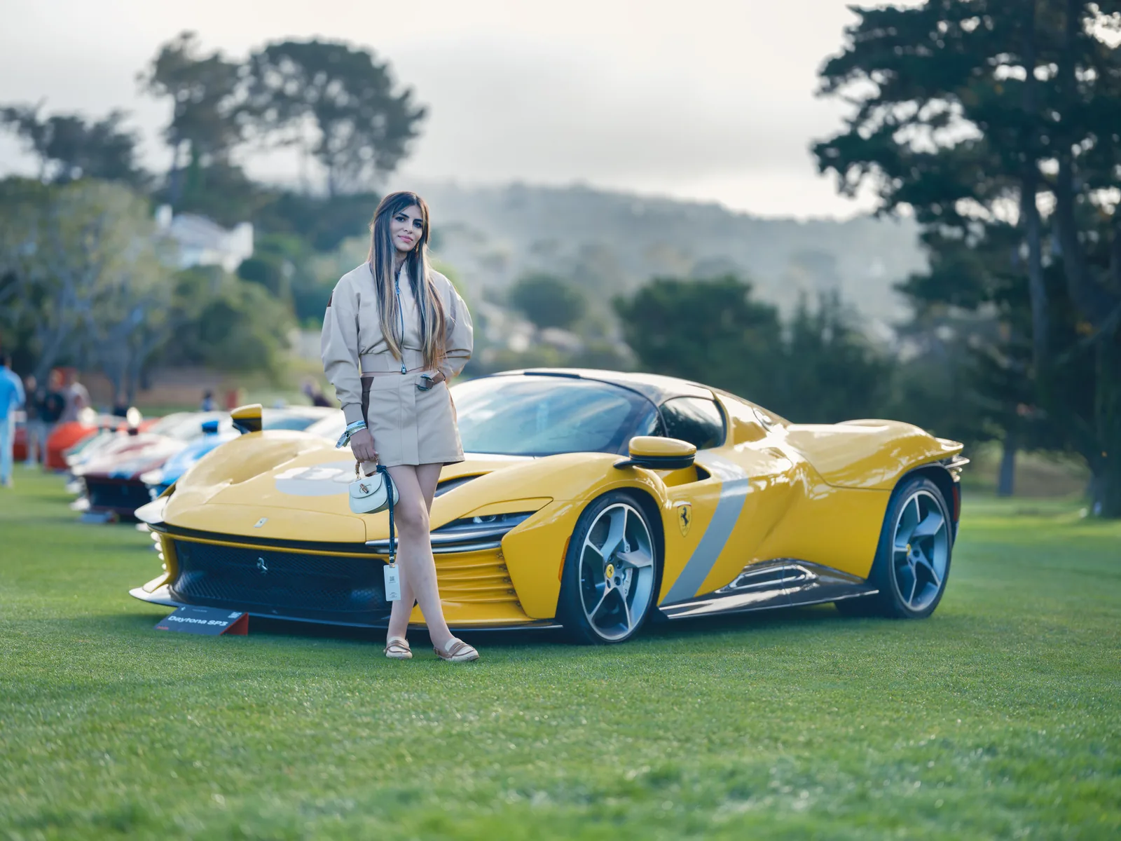 Yellow supercar on the lawn at Monterey Car Week with a model standing beside it, automotive photography by Manny Espinoza